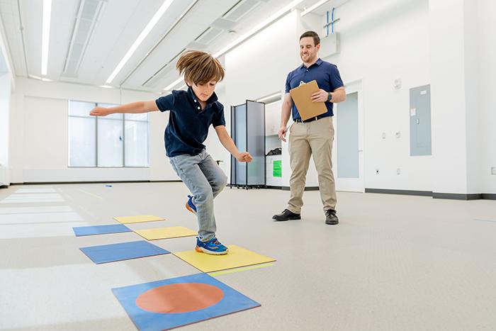 Child study subject doing hopscotch task while Postdoc Nick Fears looks on