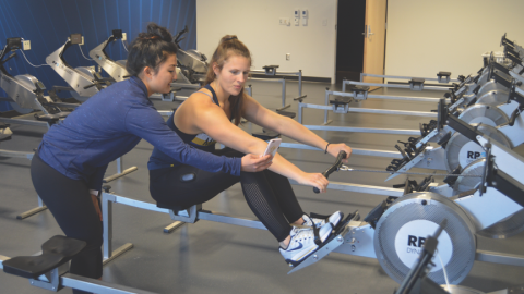 A movement science student shows a young woman on a rowing machine her smart phone